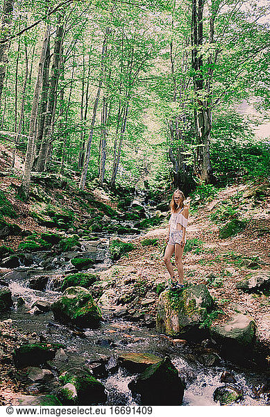 Happy tourist girl teenager in forest near to the cold fresh stream river at the waterfall Shypit  cascade in Pylypets in the forest. Carpathian Mountains