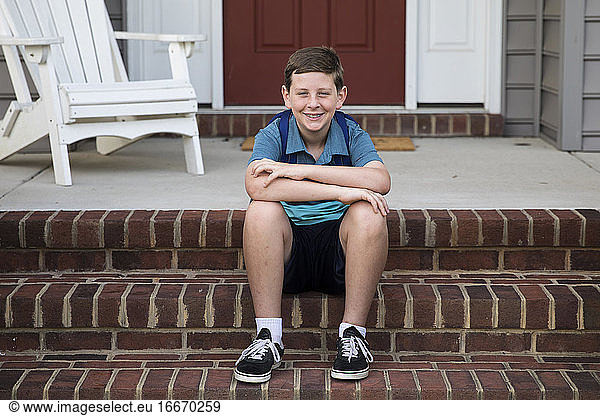 Happy Tween Boy sitzt auf Ziegelstein Front Steps
