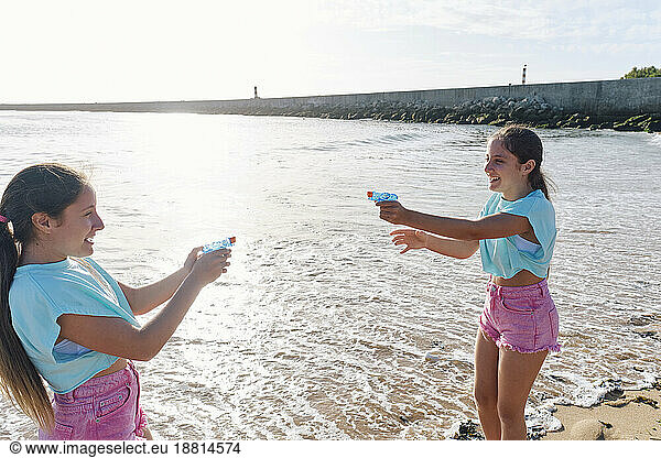 Happy twin sisters playing with squirt guns at beach