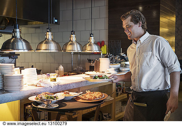 Happy waiter holding dish in commercial kitchen