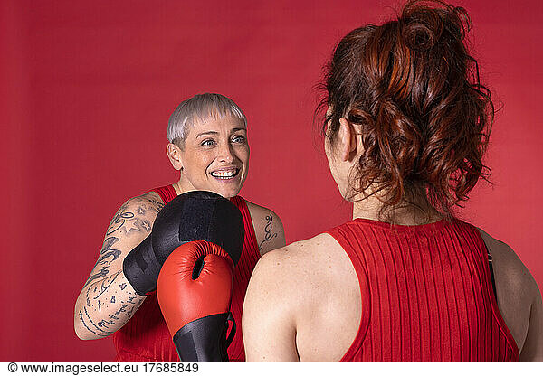Happy woman boxing with friend against red background