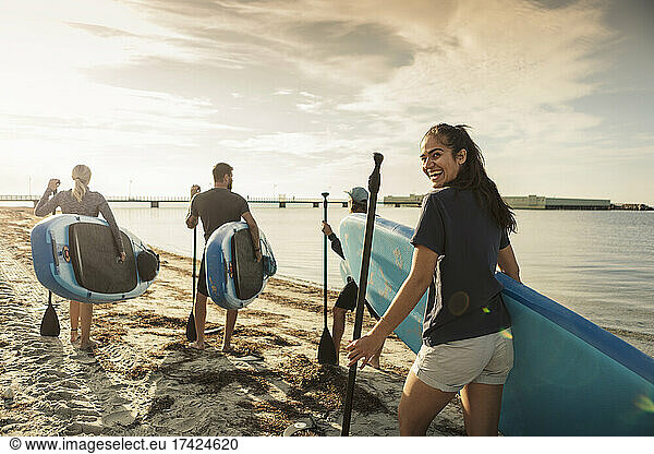 Happy woman carrying paddleboard while walking with friends at beach