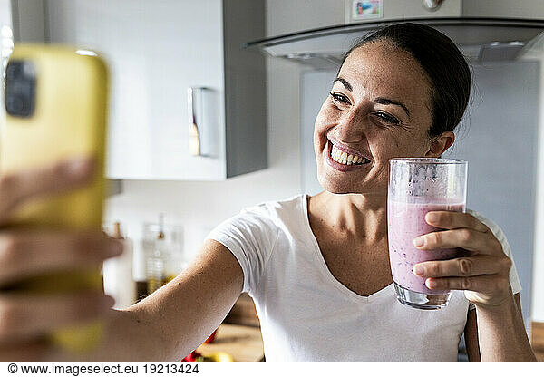 Happy woman clicking selfie with milkshake at home