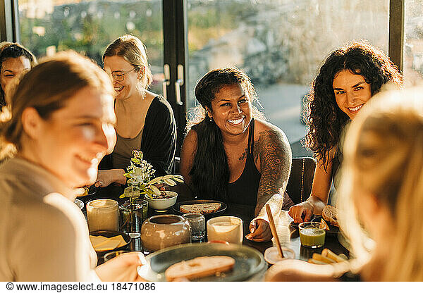 Happy woman communicating with female friends during breakfast at retreat center