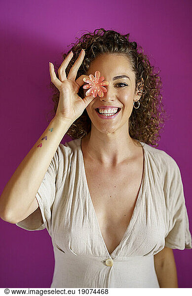 Happy woman covering eye with flower against magenta background