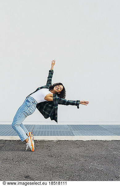 Happy woman dancing and bending over backwards in front of wall