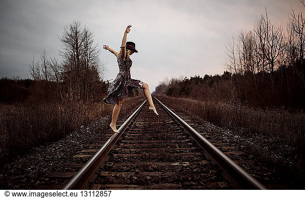 Happy woman dancing on railroad tracks against cloudy sky during sunset