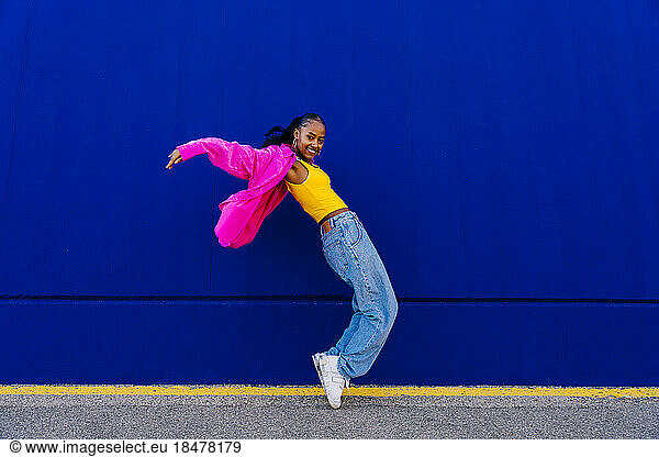 Happy woman dancing on tiptoe by blue wall