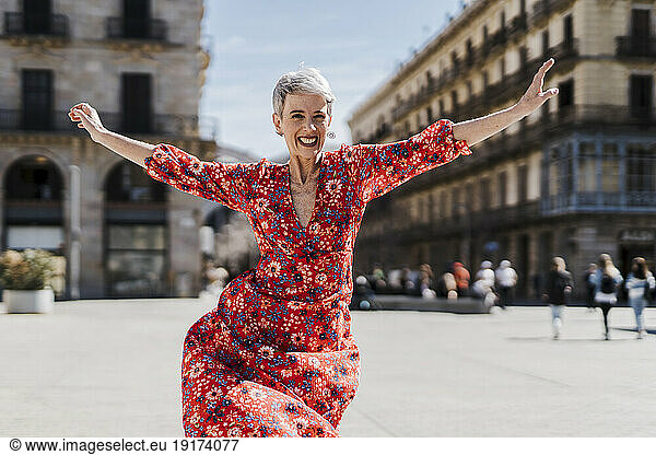 Happy woman dancing with arms outstretched in city