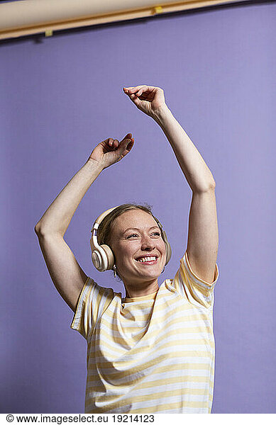 Happy woman dancing with arms raised and enjoying music on headphones in studio
