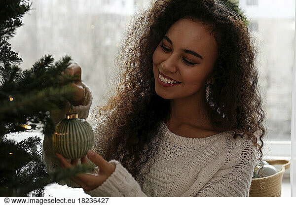 Happy woman decorating Christmas tree with bauble at home