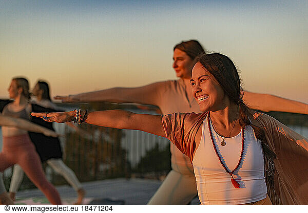 Happy woman doing yoga with female friend on patio at sunset