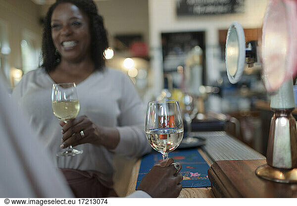 Happy woman drinking white wine with friend in bar