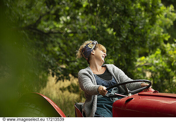 Happy woman driving tractor in orchard