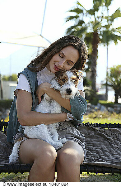 Happy woman embracing cute puppy sitting on hammock in park