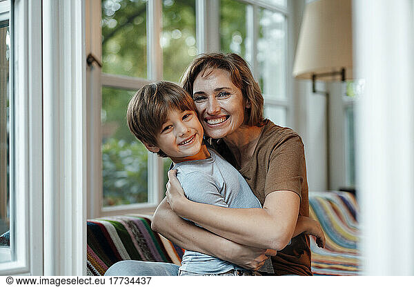 Happy woman embracing son sitting on sofa at home