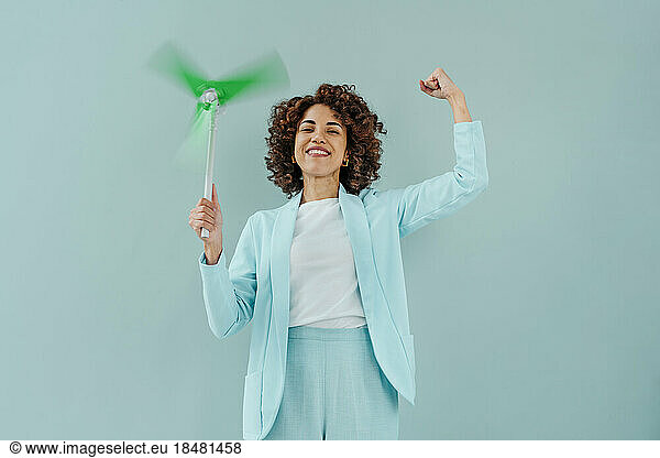 Happy woman flexing muscles and holding wind turbine spinning against blue background