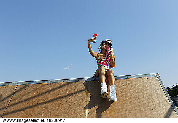 Happy woman gesturing and taking selfie through mobile phone on rooftop of house