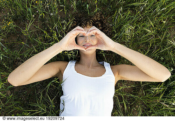 Happy woman gesturing heart shape lying on grass