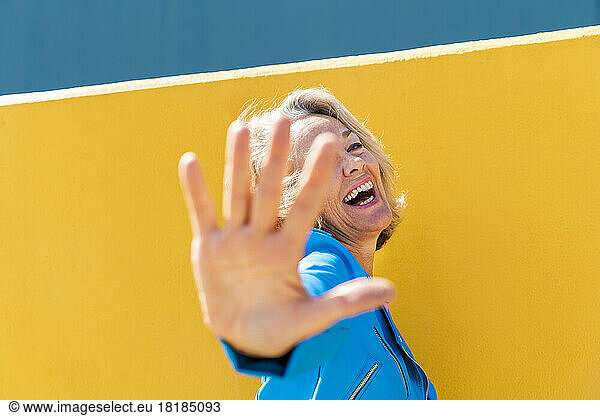 Happy woman gesturing in front of colored wall