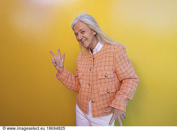 Happy woman gesturing in front of yellow wall