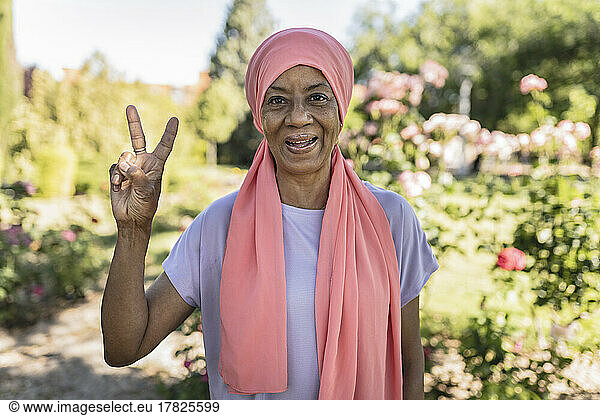 Happy woman gesturing peace sign in public park