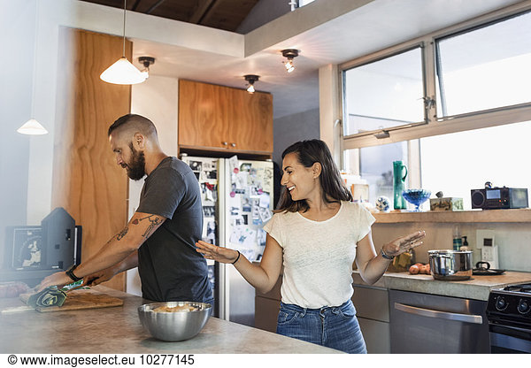 Happy woman gesturing while talking to man cutting vegetables in kitchen