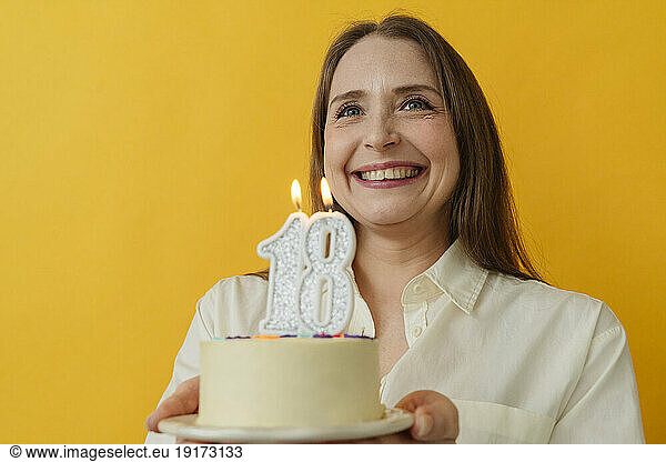 Happy woman holding birthday cake against yellow background