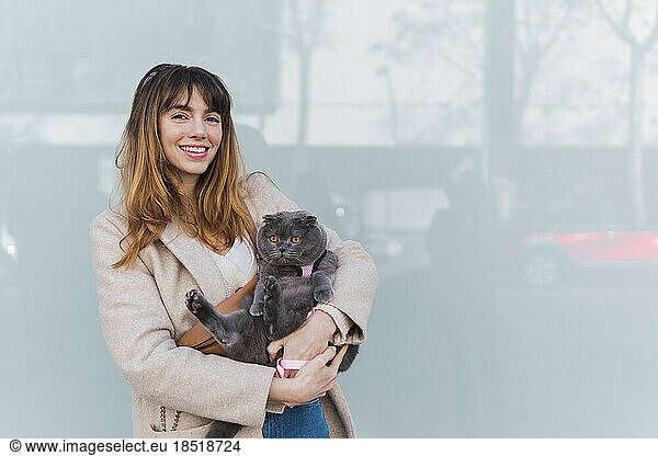 Happy woman holding cat standing in front at wall