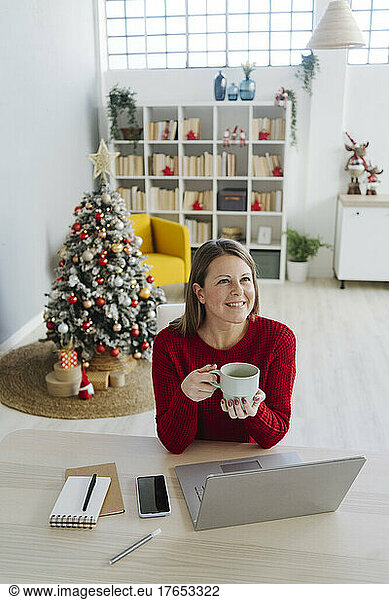 Happy woman holding coffee cup sitting at table in living room
