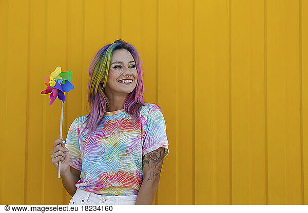 Happy woman holding colorful pinwheel toy in front of yellow wall