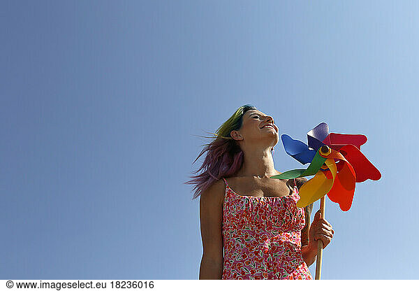 Happy woman holding colorful pinwheel toy under blue sky