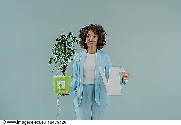 Happy woman holding electric plug inserted in potted plant and watering can