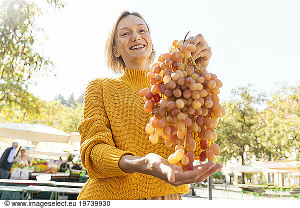 Happy woman holding fresh bunch of grapes at farmer's market