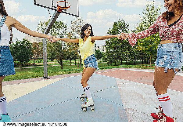 Happy woman holding hands of friends roller skating at sports court