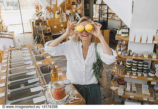 Happy woman holding lemons over eyes at store