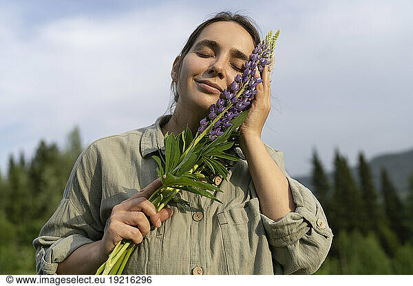 Happy woman holding lupine flowers under sky
