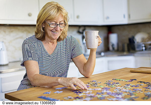 Happy woman holding mug while playing jigsaw puzzle at home