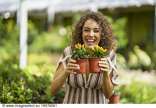 Happy woman holding red and yellow pepper plants in nursery