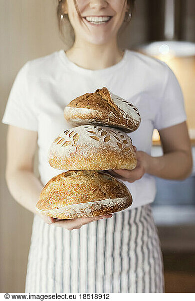 Happy woman holding stack of sourgough breads at home