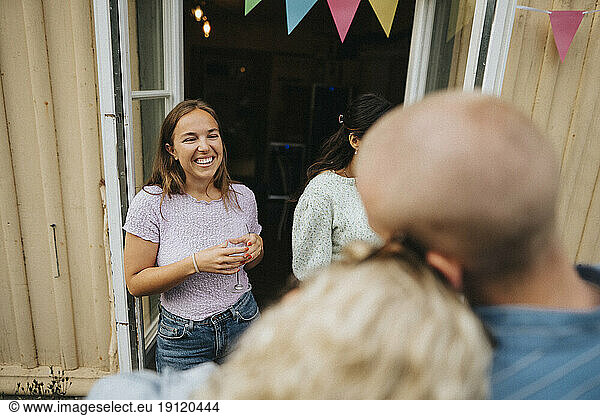 Happy woman holding wineglass while enjoying with friends during dinner party at cafe