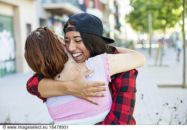 Happy woman hugging lesbian on footpath
