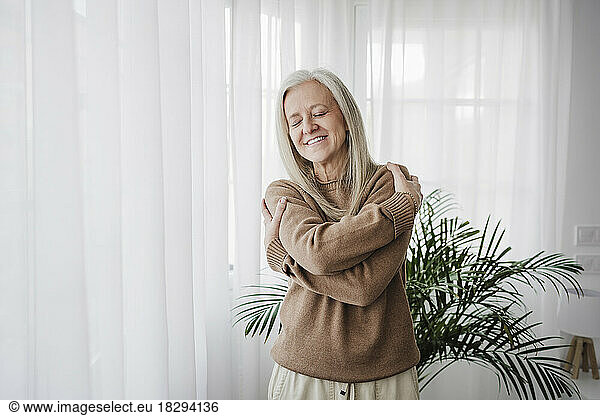 Happy woman hugging self standing at home