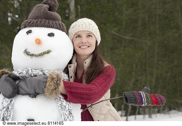 Happy woman hugging snowman in woods