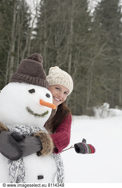 Happy woman hugging snowman in woods