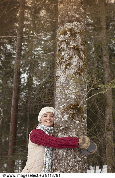 Happy woman hugging tree trunk in woods