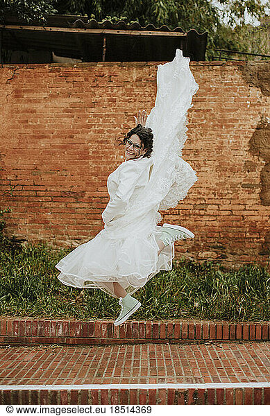Happy woman in wedding dress jumping on footpath