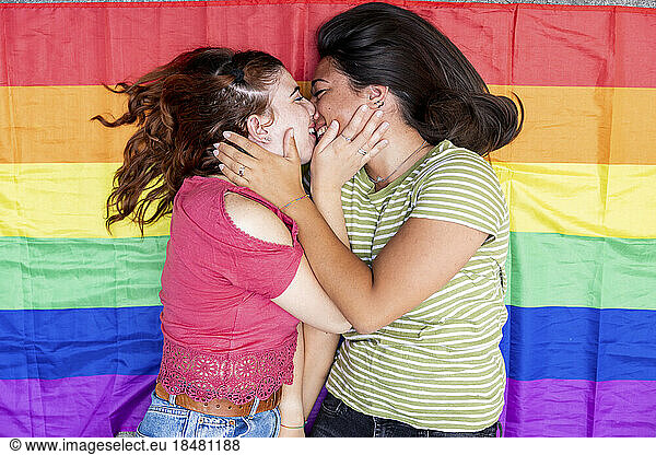 Happy woman kissing girlfriend lying on rainbow flag