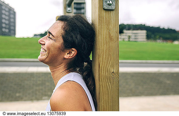 Happy woman leaning against gymnastics bar at park