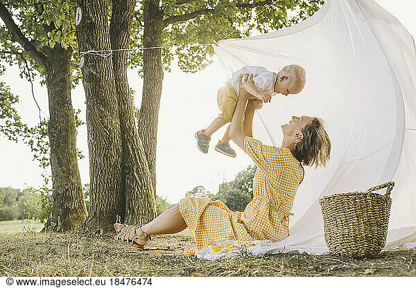 Happy woman lifting son under tree at park